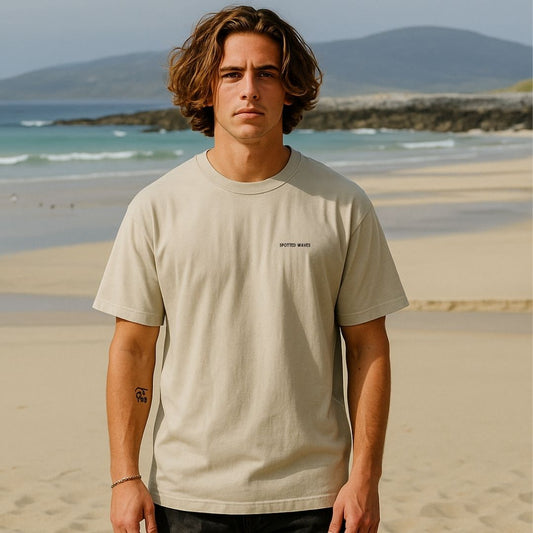 Man wearing a beige t-shirt on a beach with mountains in the background