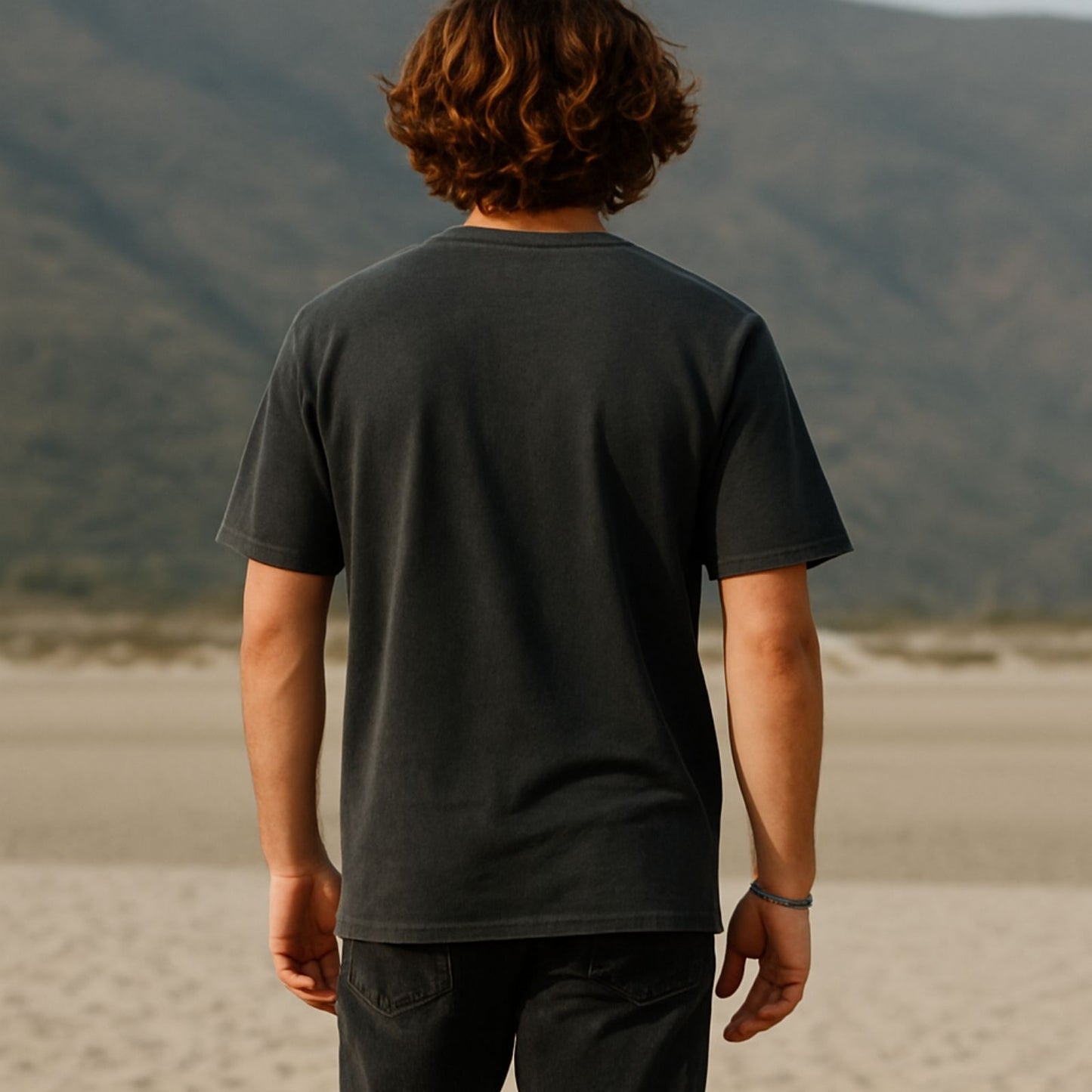 Person wearing a black t-shirt standing in a desert landscape with mountains in the background
