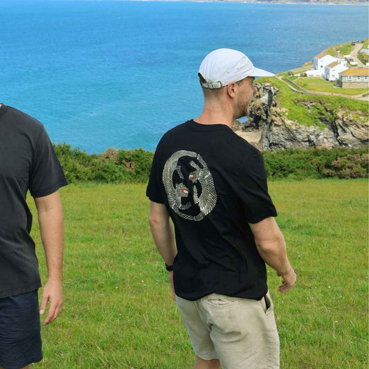 Two men standing on a grassy hill overlooking a blue sea with a coastal landscape.