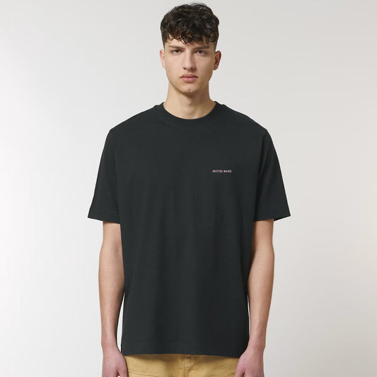 Person wearing a black t-shirt with a small logo on a plain background