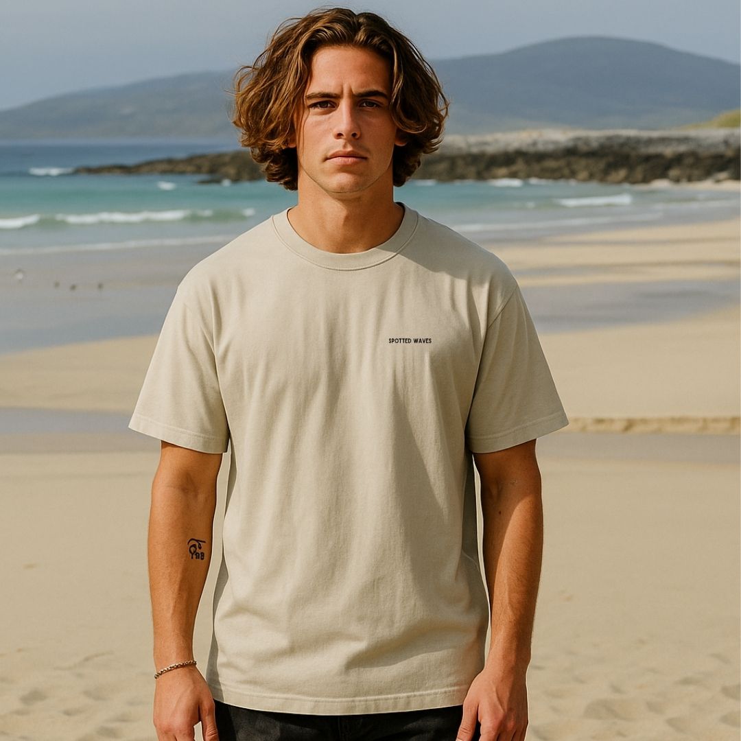 Man wearing a beige t-shirt on a beach with mountains in the background