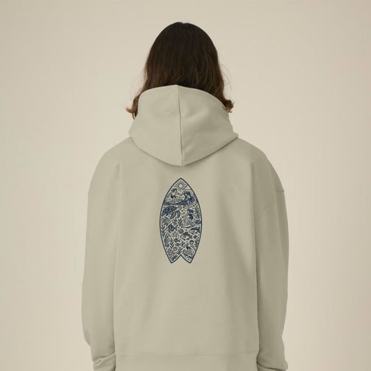 Person wearing a sand hoodie with a surf board design n the back against a beige background