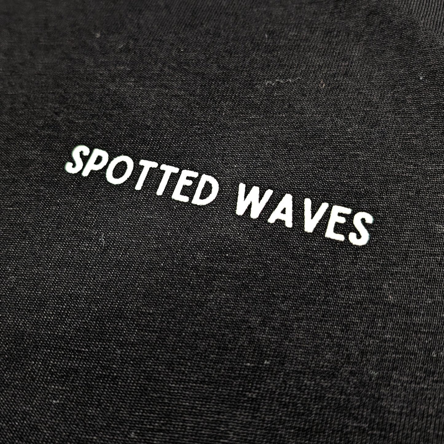 Black fabric with 'SPOTTED WAVES' text embroidered on it