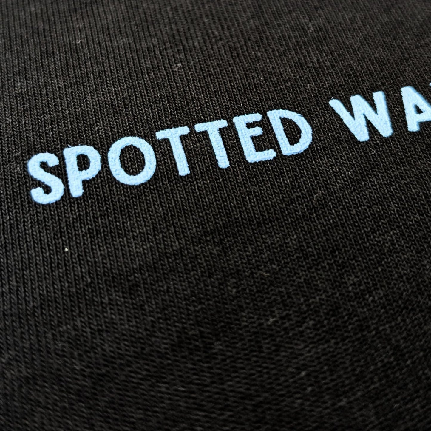 Black fabric with 'SPOTTED WAVES' embroidered in white