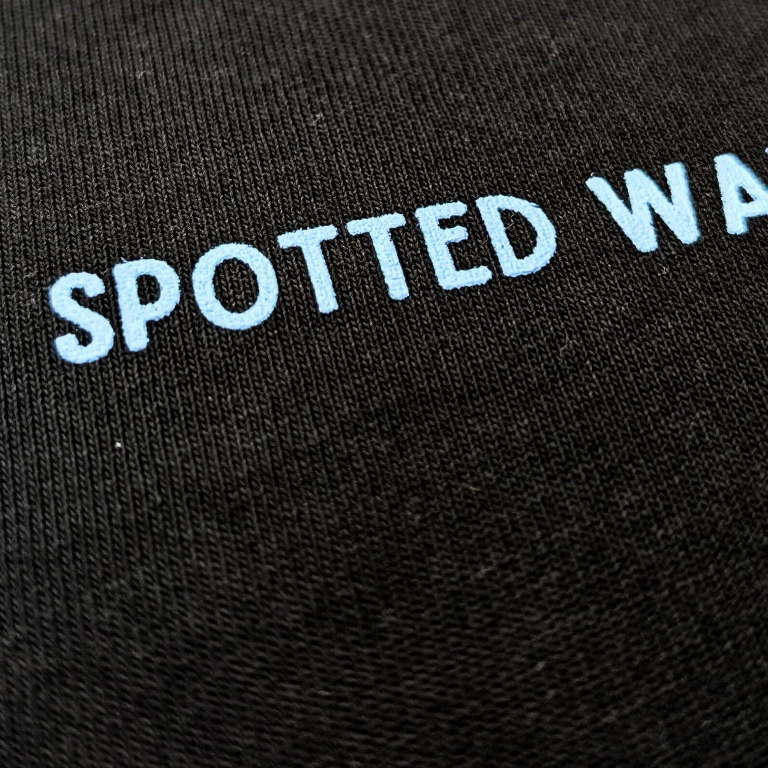 Black fabric with 'SPOTTED WAVES' embroidered in white