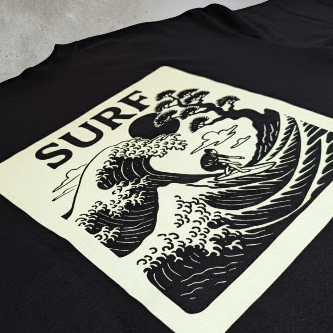 Black t-shirt with a graphic design featuring a wave and text on a concrete surface
