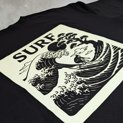 Black t-shirt with a graphic design featuring a wave and text on a concrete surface