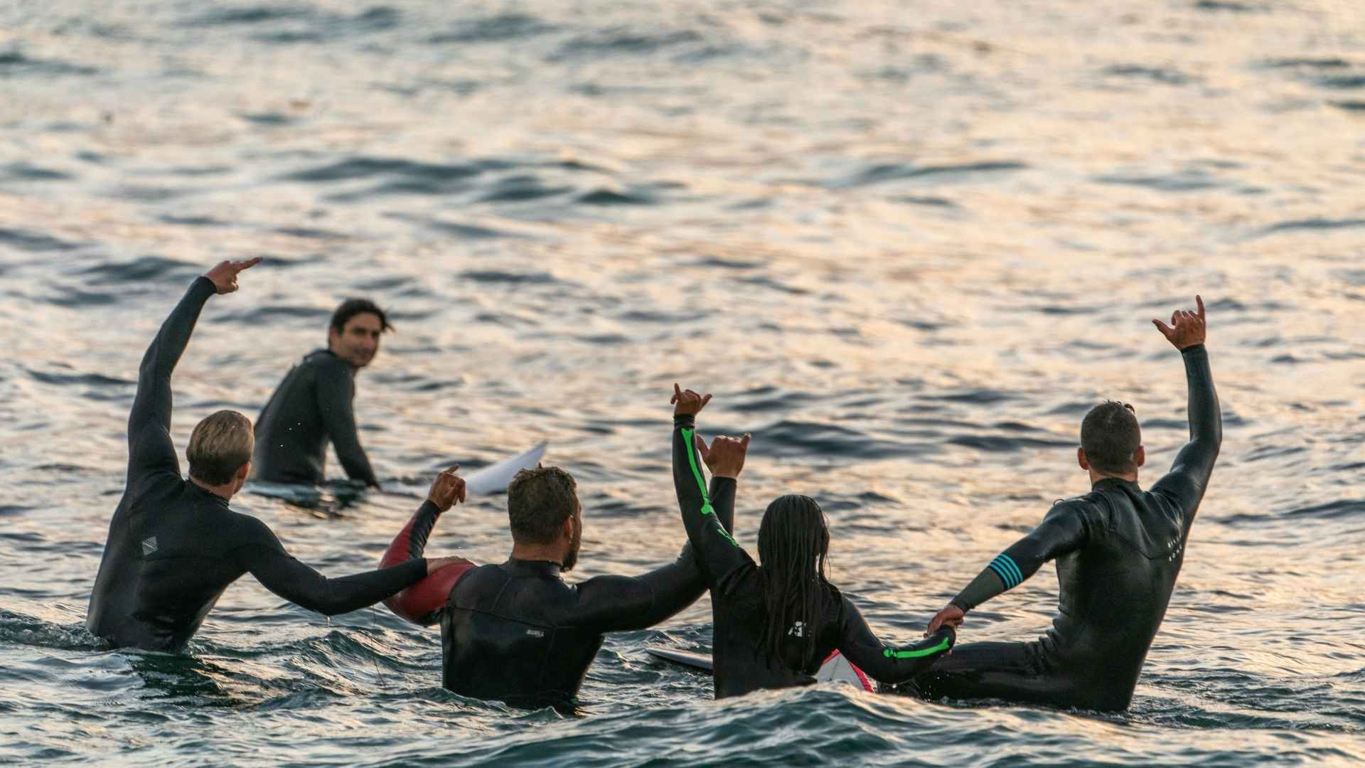 Group of people in wetsuits with arms raised in the air on a body of water.